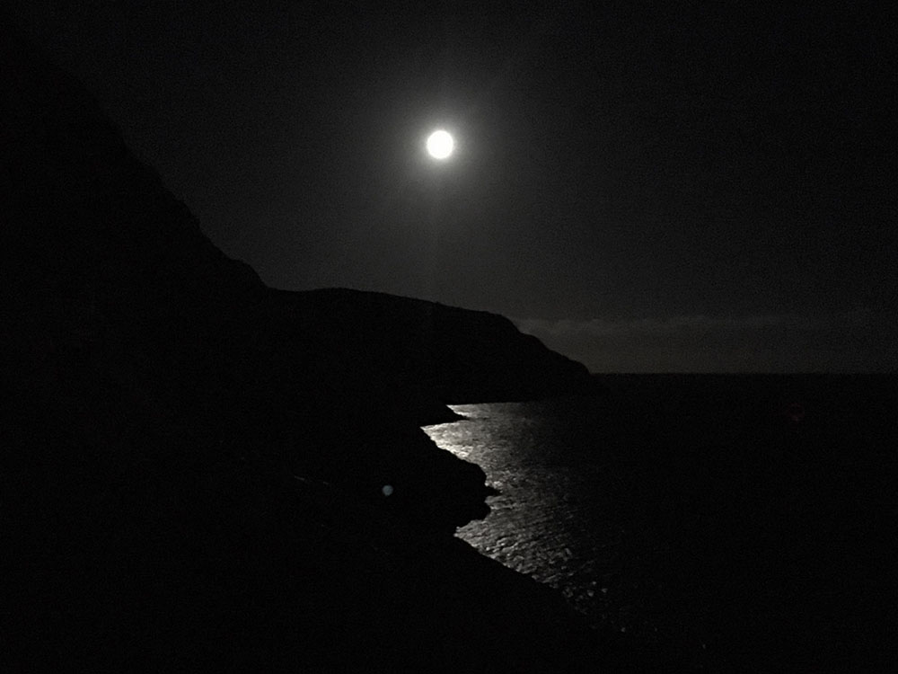 The moon gleaming behind the dark hillside.